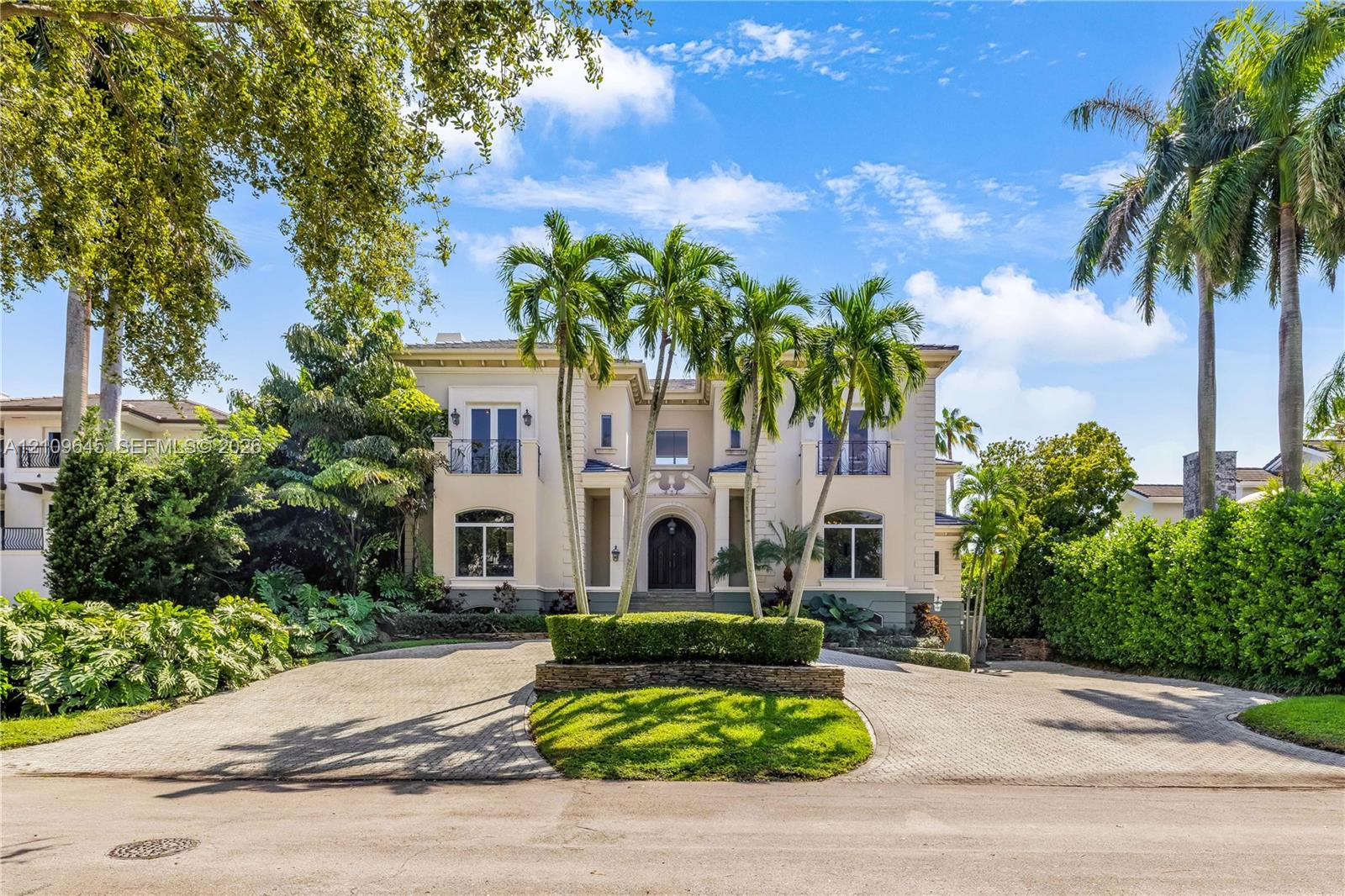 Two-story Mediterranean-style exterior featuring a stucco facade, arched entryway, upper-level balconies with wrought-iron railings, and a circular paved driveway