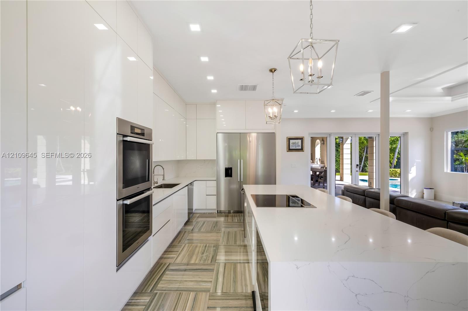 Kitchen featuring high-gloss cabinetry, stone-surfaced center island with integrated cooktop, built-in stainless steel double ovens, recessed lighting, and patterned tile flooring