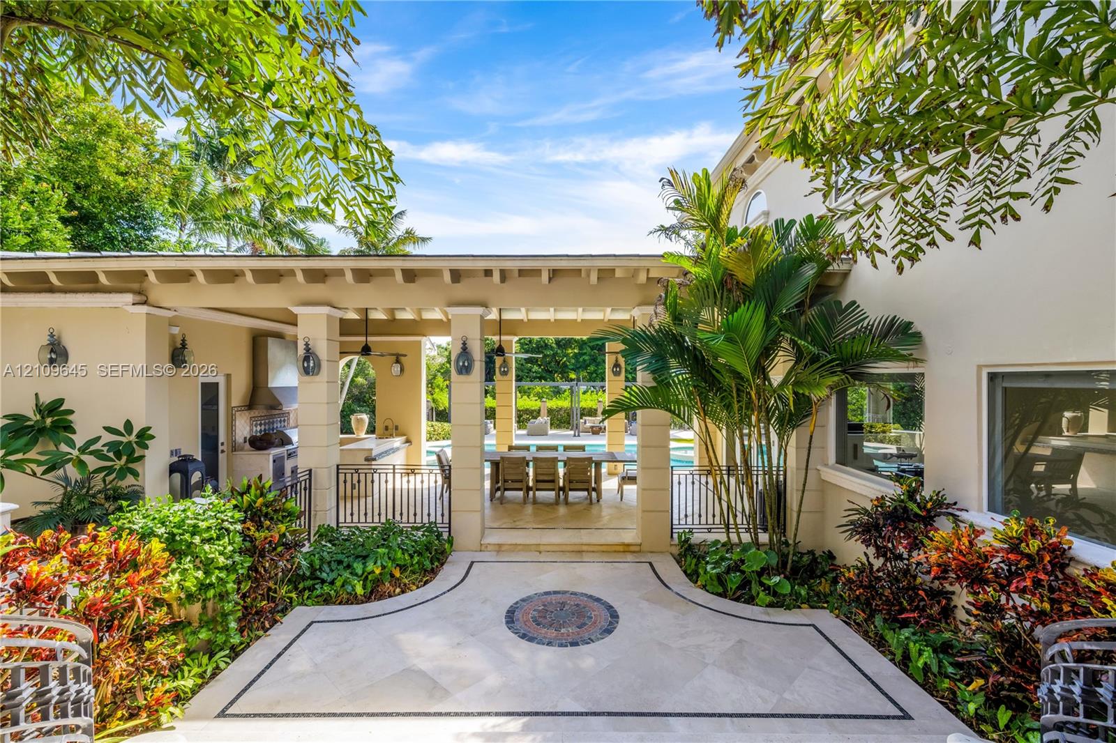 Covered lanai featuring a stone-paver patio with decorative inlay, built-in outdoor kitchen with stainless steel ventilation hood, and heavy-timber beam ceiling