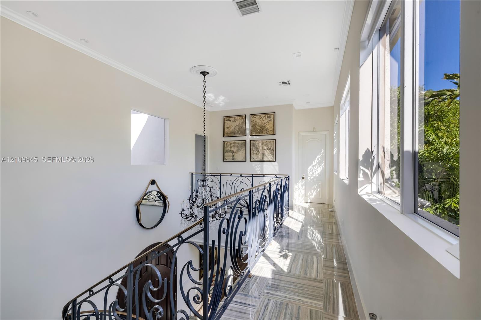 Hallway featuring large-format tile flooring, ornate wrought-iron railings, high ceilings with recessed lighting, and a multi-tiered crystal chandelier