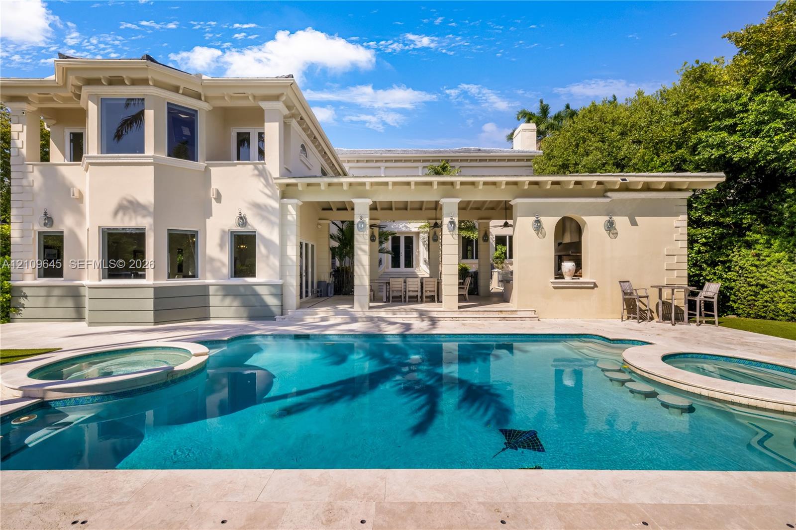 Stucco exterior featuring a covered patio, swimming pool with integrated spa, and stone-finished pool decking