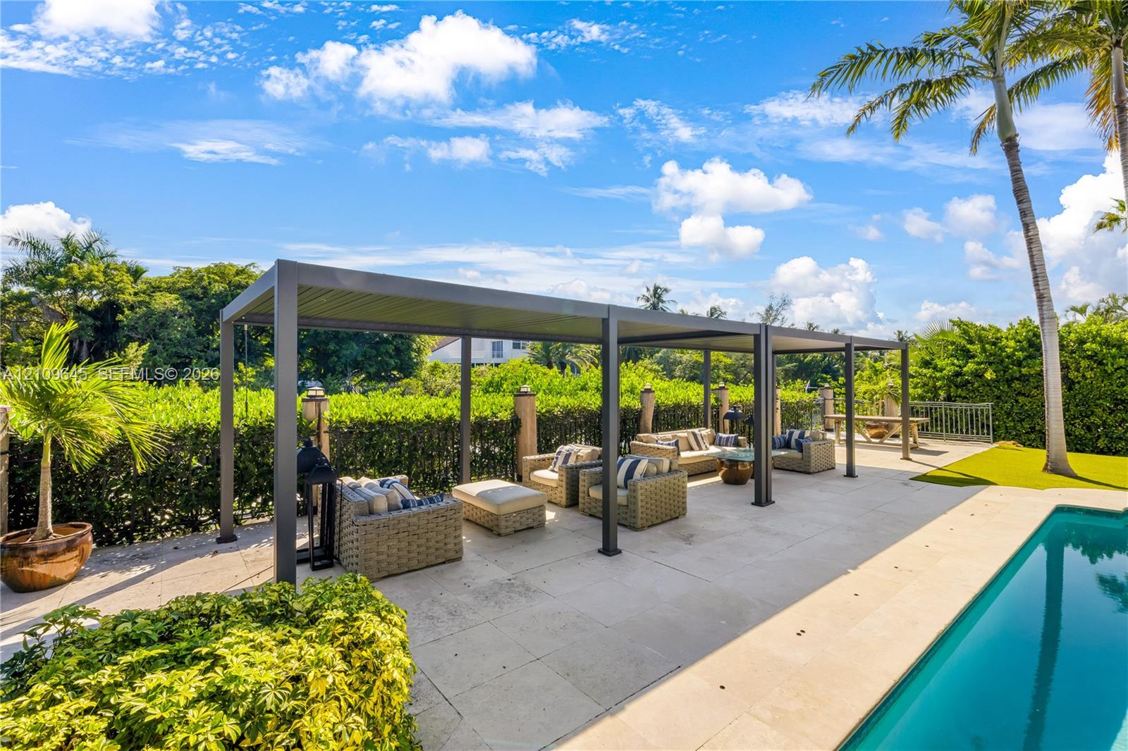 Outdoor living space featuring a modern metal pergola, paved stone pool deck, and inground swimming pool surrounded by mature landscape hedging