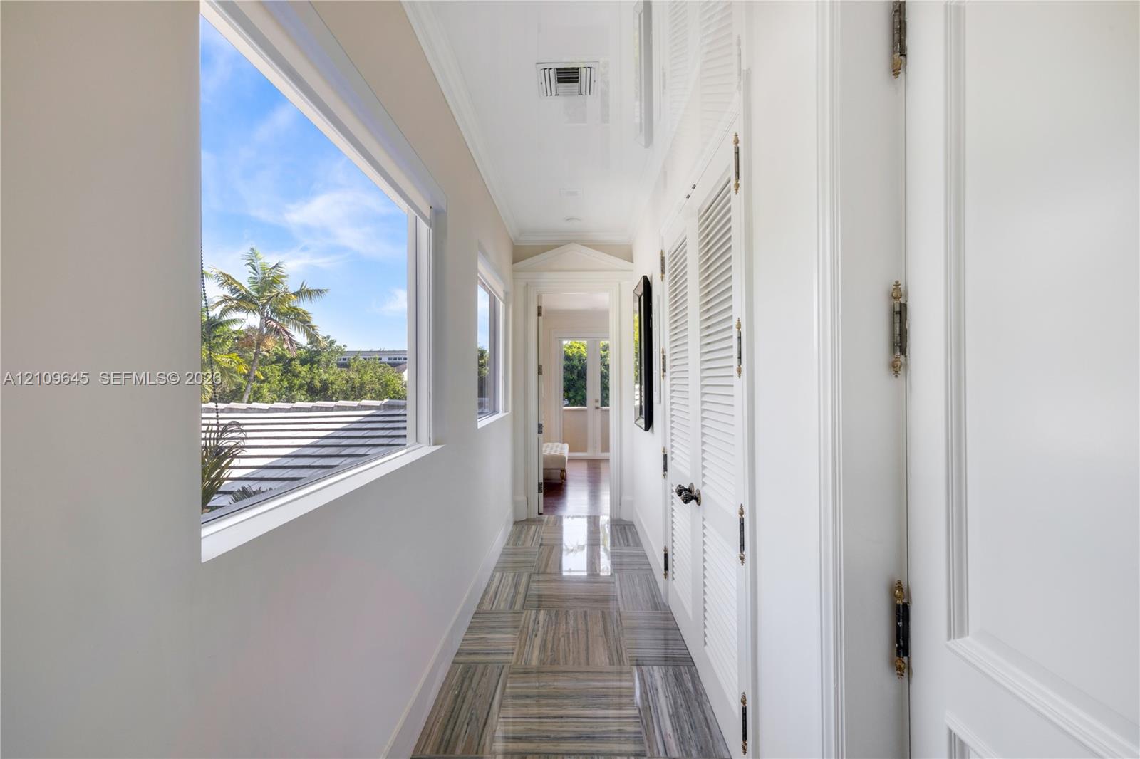 Hallway featuring polished stone flooring, louvered closet doors, crown molding, and large windows