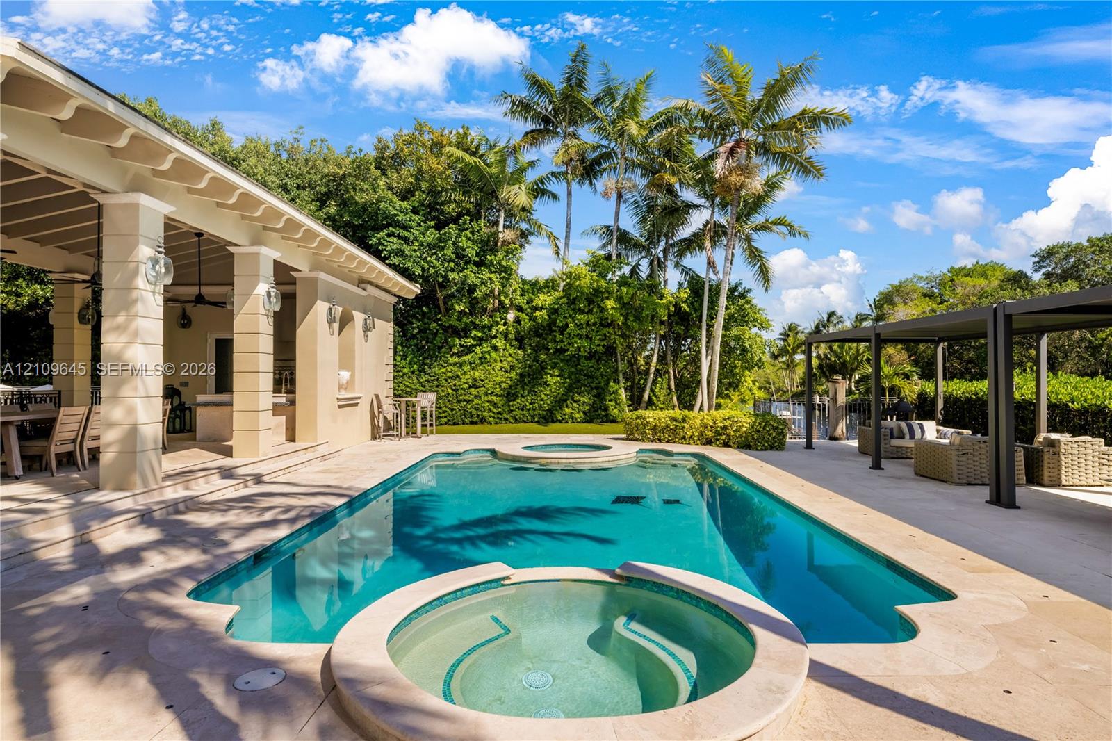 Swimming pool with integrated spa, covered lanai featuring structural columns, paver decking, and metal pergola
