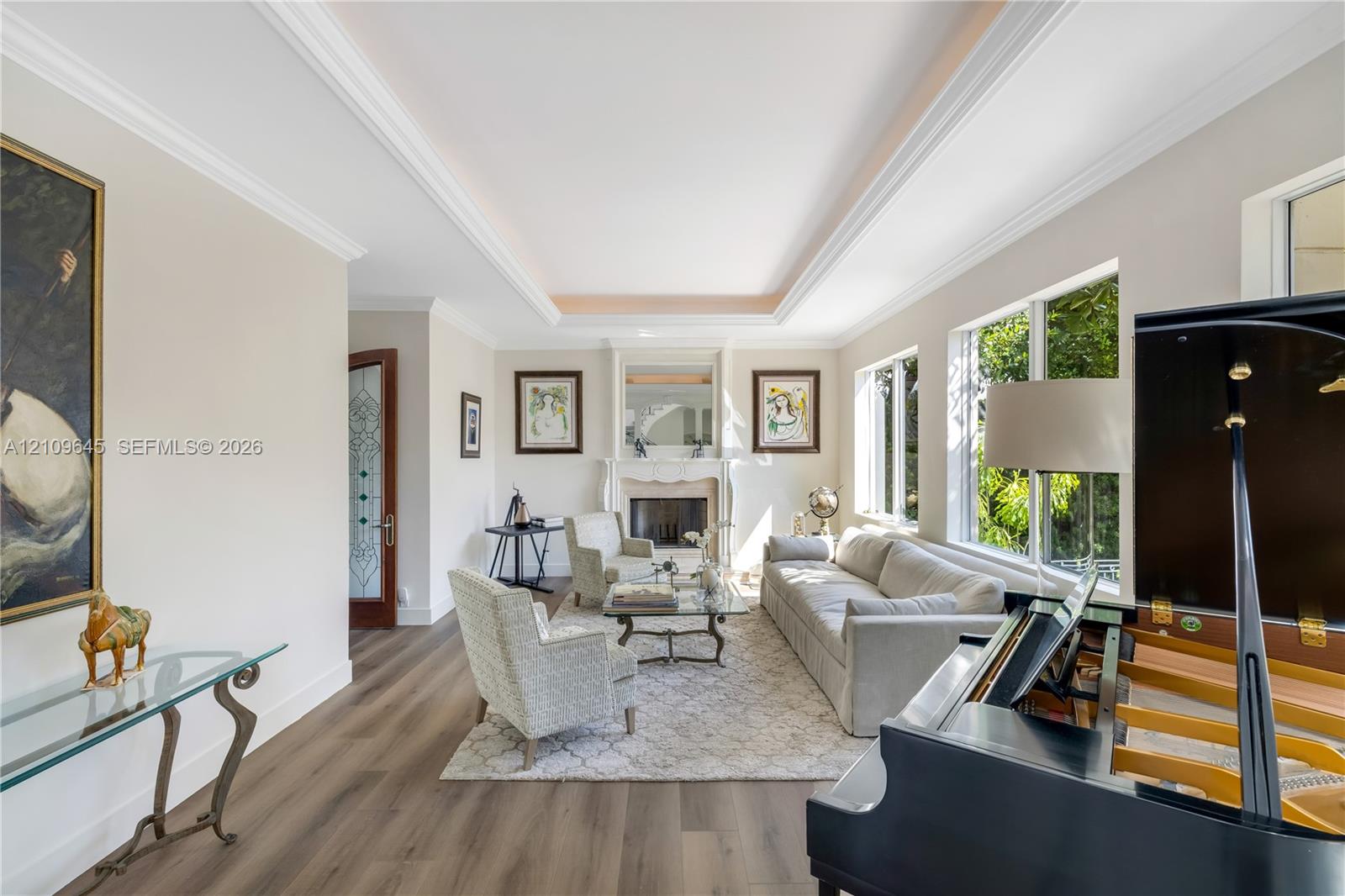 Living area featuring a tray ceiling, wood-finish flooring, a traditional fireplace with a decorative mantel, and multi-pane windows