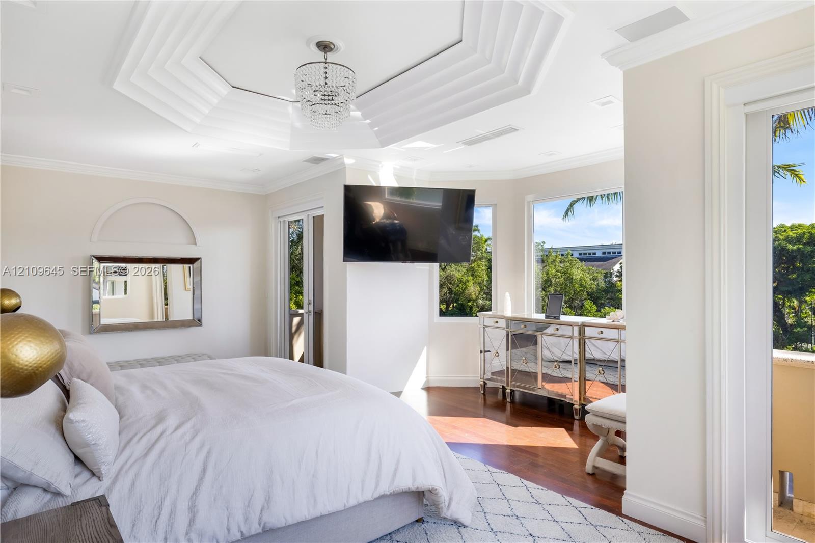 Octagonal tray ceiling featuring crown molding and a crystal chandelier, wood-finish flooring, and large windows with exterior foliage
