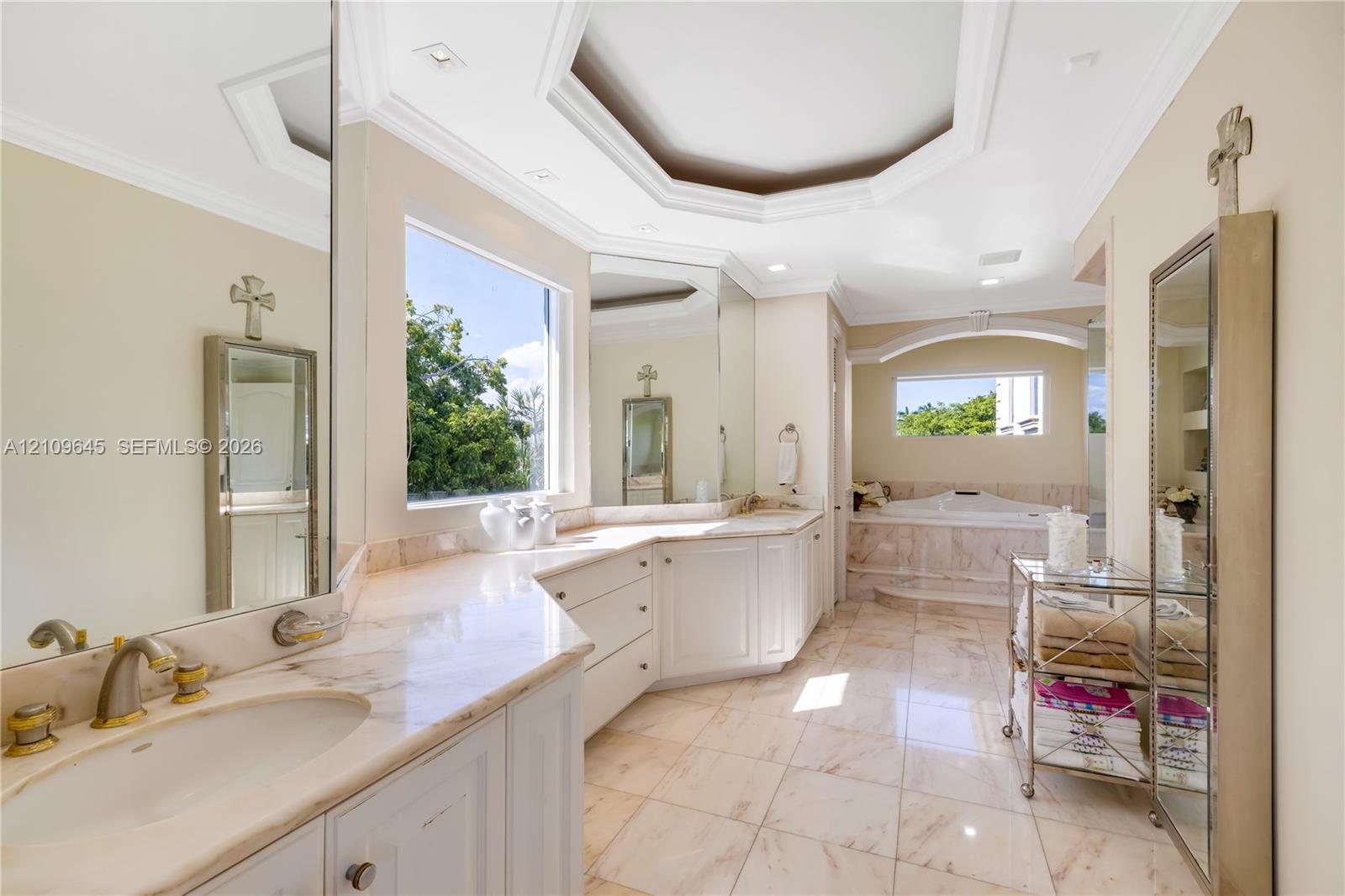 Bathroom featuring stone-finish flooring, white built-in cabinetry with stone countertops, an inset soaking tub with a stone surround, and an octagonal tray ceiling