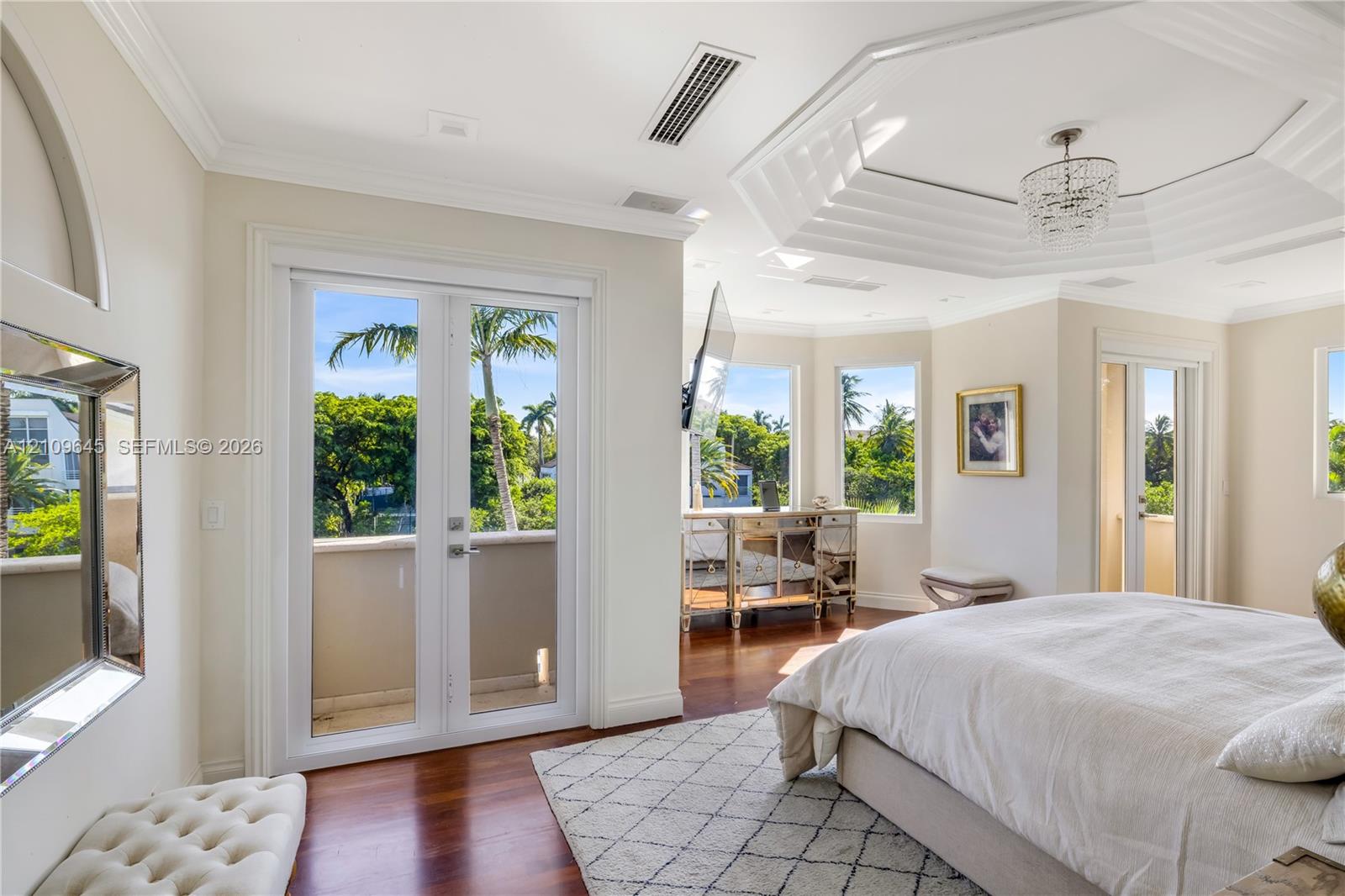Octagonal tray ceiling with inset crown molding, polished wood-finish flooring, dual-pane glass entry doors, and multi-light crystal chandelier