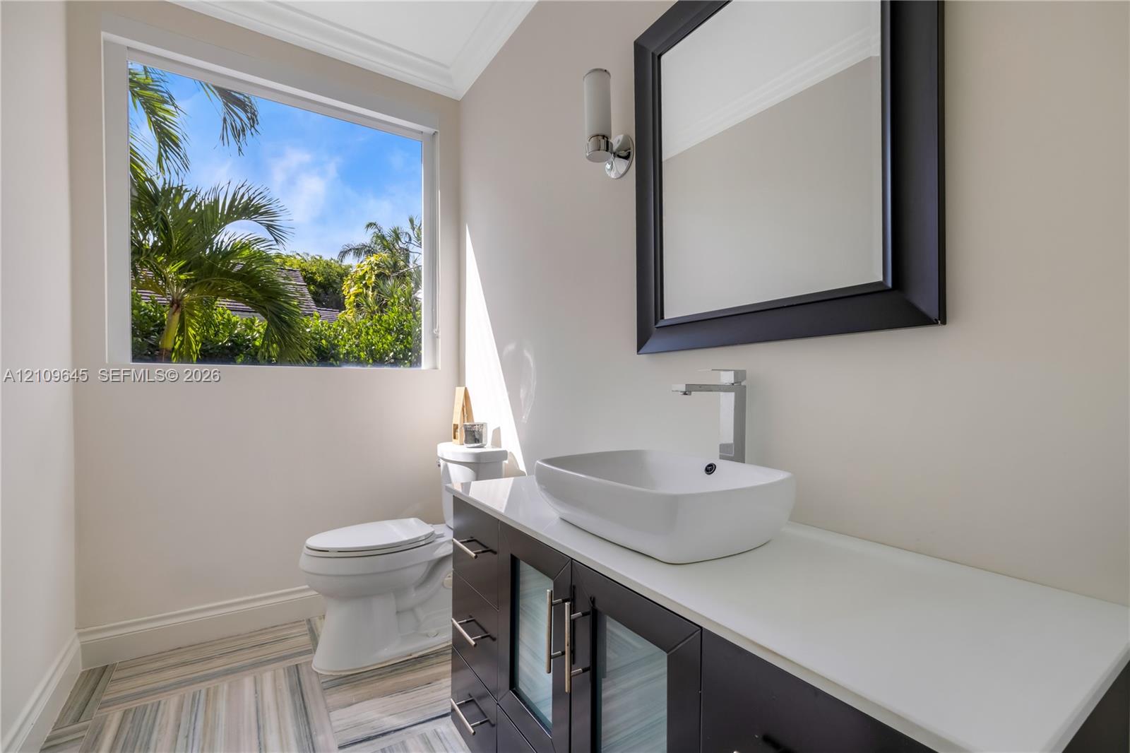 Modern vanity featuring a stone countertop, vessel sink, and metallic hardware, complemented by patterned tile flooring and a wall-mounted light fixture