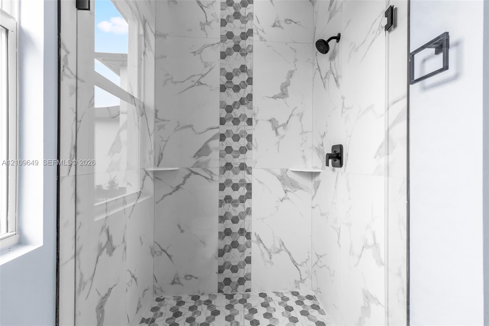Walk-in shower featuring large-format stone-patterned wall tiles, a vertical decorative hexagonal tile inlay, a matching hexagonal tile floor, a glass enclosure, and matte black fixtures
