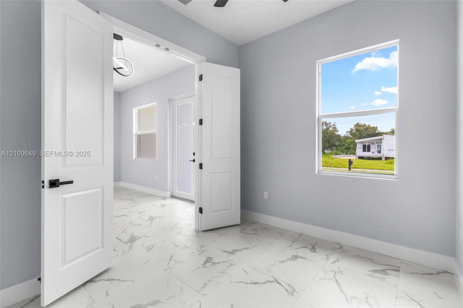 Large-format white tile flooring with grey veining, crisp neutral wall paint, multi-panel double doors with matte black hardware, and double-pane window