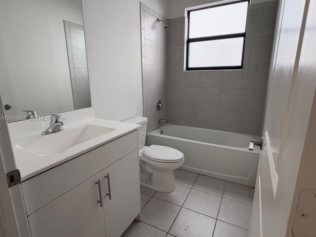 Bathroom featuring a white vanity cabinet with an integrated basin, wall-to-wall mirror, tiled flooring, and a bathtub with a tiled surround Bathroom featuring a white vanity cabinet with an integrated basin, wall-to-wall mirror, tiled flooring, and a bathtub with a tiled surround