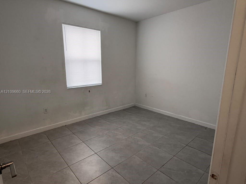 Neutral-toned tile flooring and a single-pane window with installed blinds Neutral-toned tile flooring and a single-pane window with installed blinds