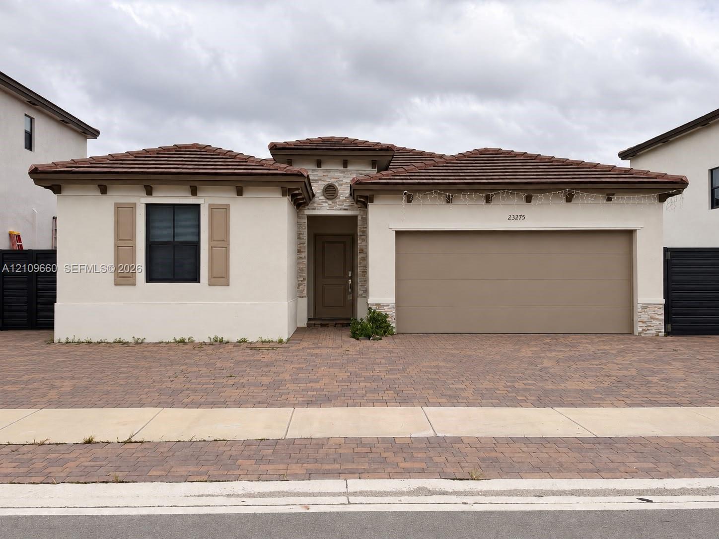 Single-story stucco exterior featuring a tile roof, stone masonry accents, exposed rafters, and a paved driveway