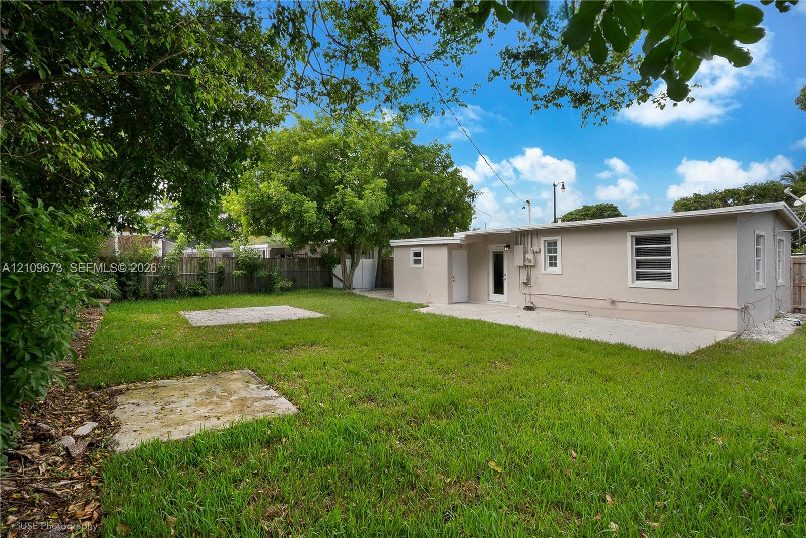 Backyard featuring a grass lawn, concrete patio, perimeter wood fencing, and mature trees