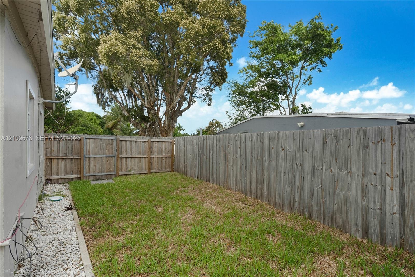 Rear exterior space featuring a grass lawn, white stone border, wood-finish privacy fencing, and a gated access point