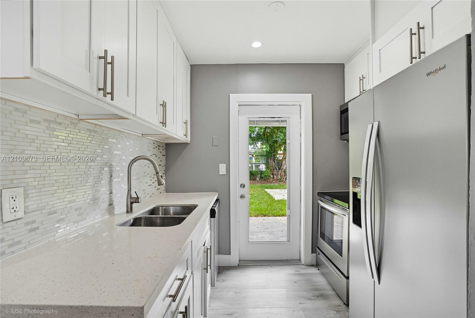 Kitchen featuring white shaker-style cabinetry, solid-surface countertops, a mosaic tile backsplash, stainless steel appliances, and wood-finish flooring