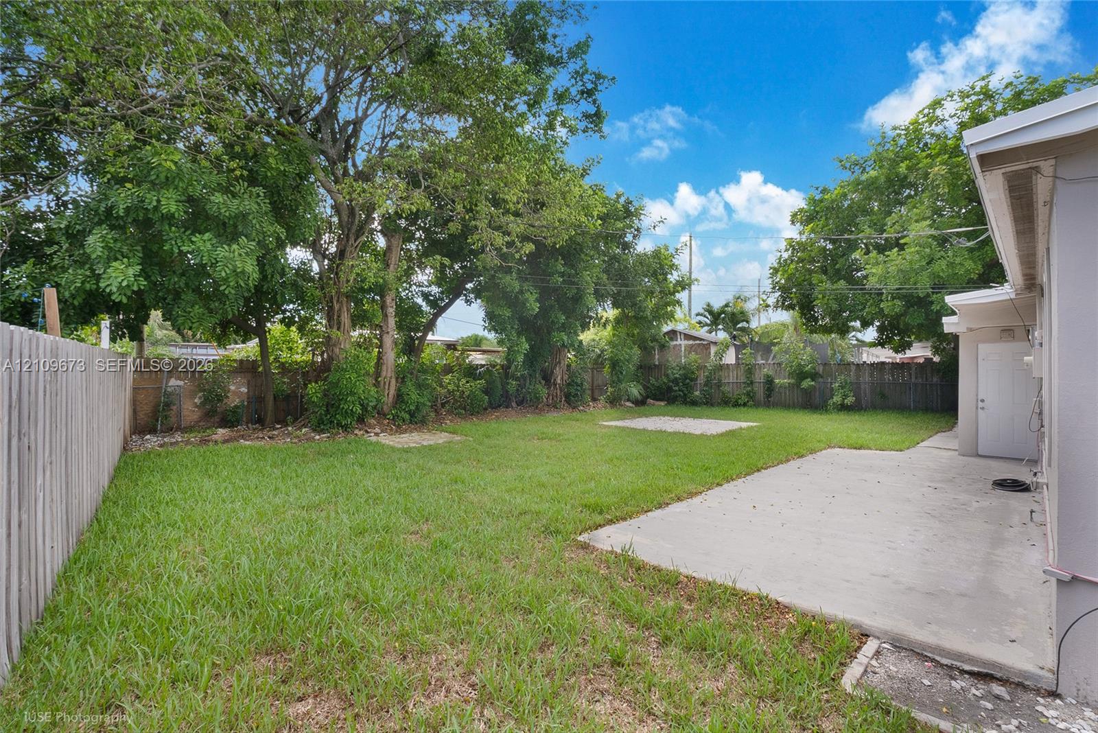 Spacious backyard featuring a concrete patio, perimeter wood fencing, and mature trees