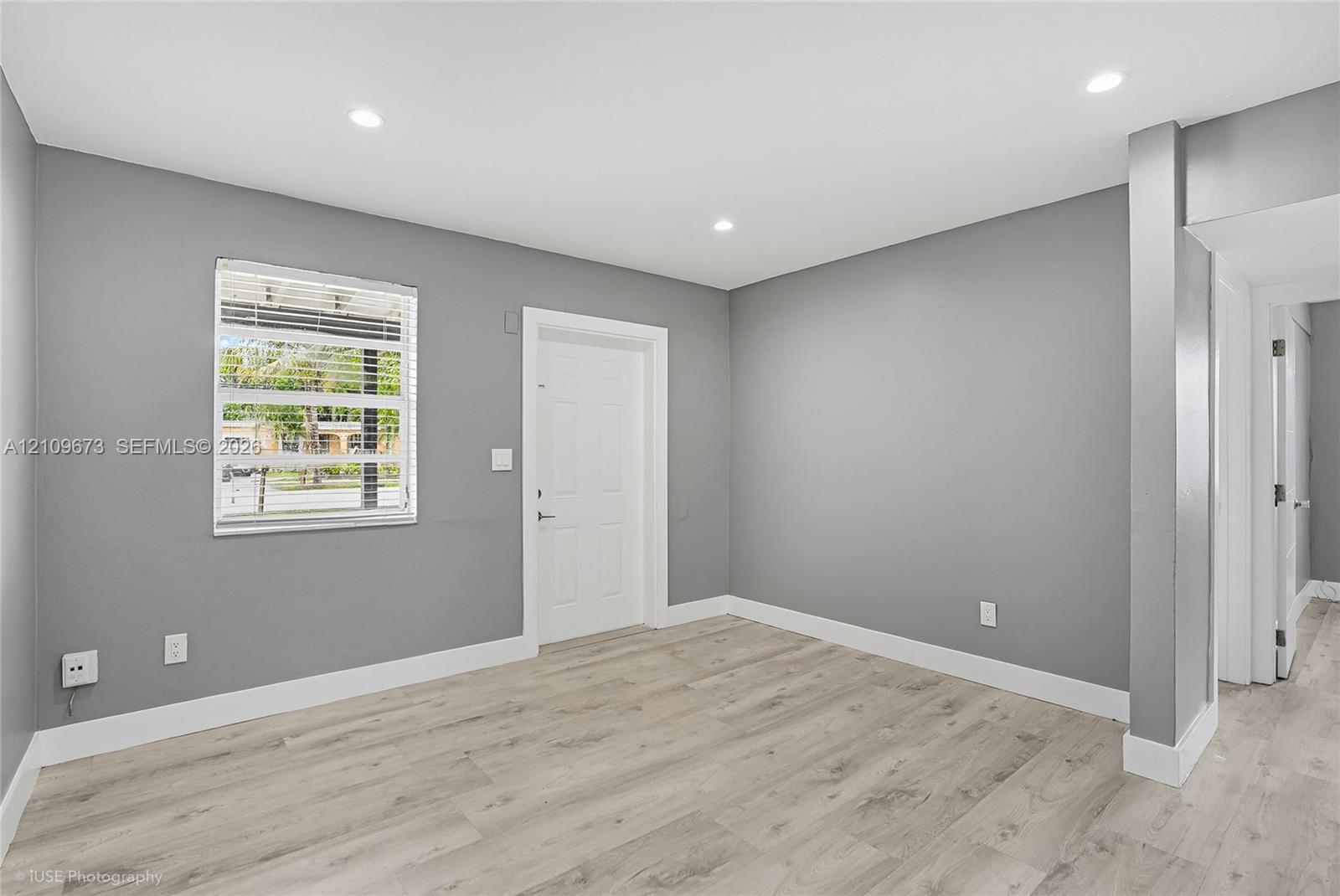 Neutral gray wall paint, light-toned wood-finish flooring, recessed ceiling lighting, and a window with horizontal blinds Neutral gray wall paint, light-toned wood-finish flooring, recessed ceiling lighting, and a window with horizontal blinds