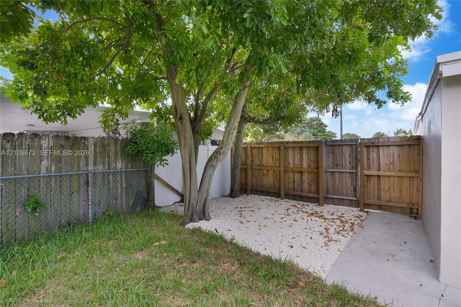 Outdoor space featuring a mature tree, gravel ground cover, a concrete walkway, and wood privacy fencing