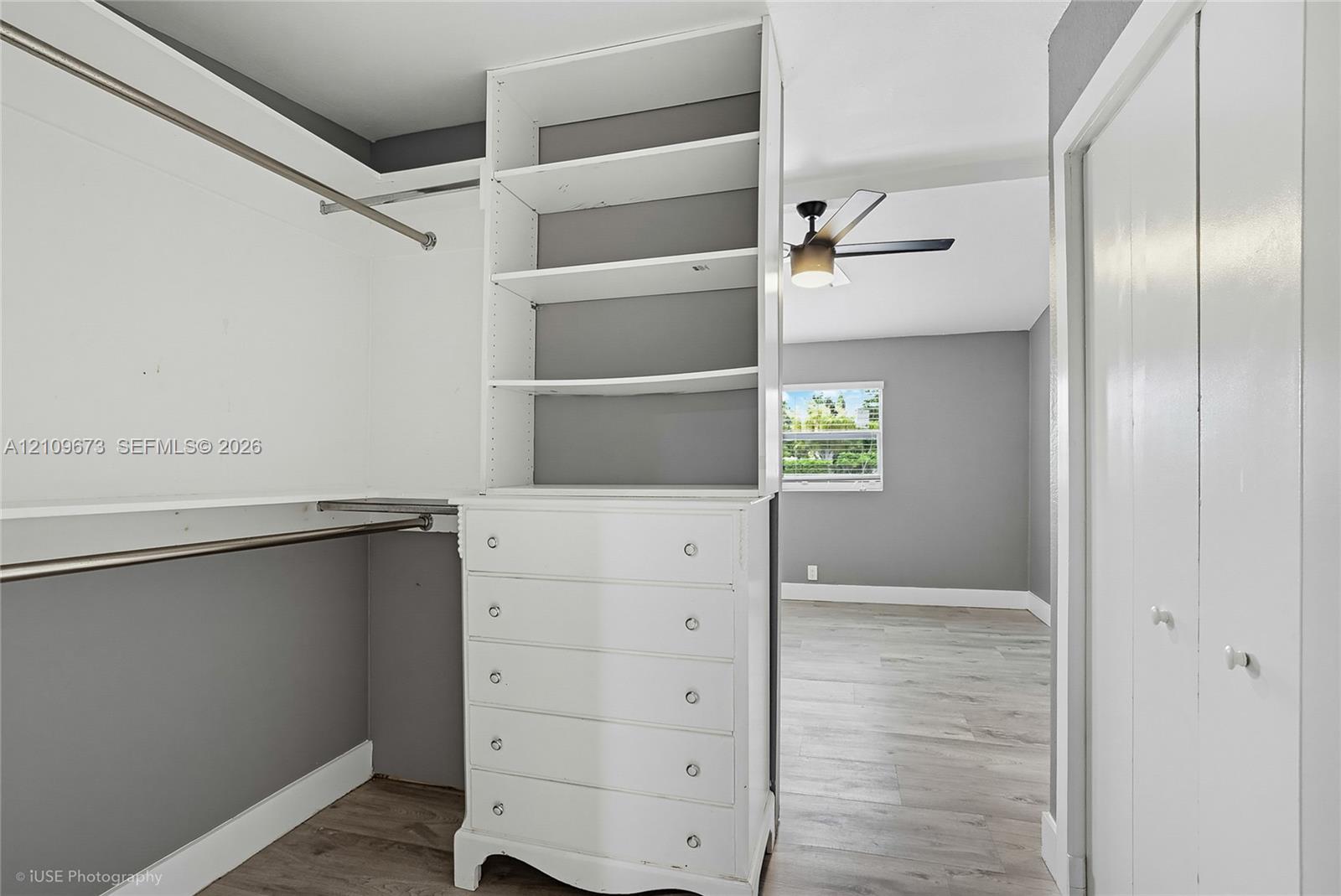 Walk-in closet featuring built-in white cabinetry with open shelving and drawers, wood-finish flooring, and dual hanging rods