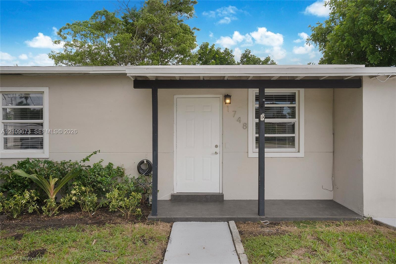 Exterior faade featuring neutral stucco siding, a covered entryway with a concrete porch, and horizontal multi-pane windows Exterior faade featuring neutral stucco siding, a covered entryway with a concrete porch, and horizontal multi-pane windows
