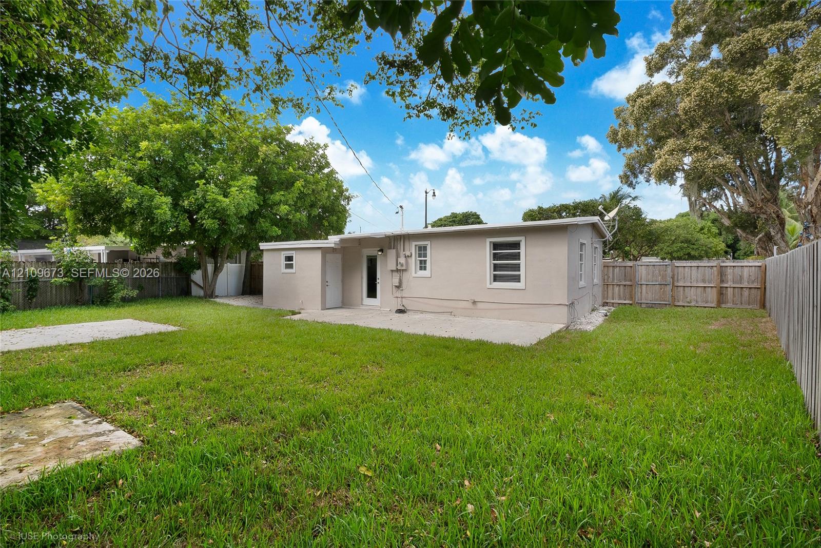 Expansive backyard featuring a concrete patio, perimeter wood fencing, and mature trees