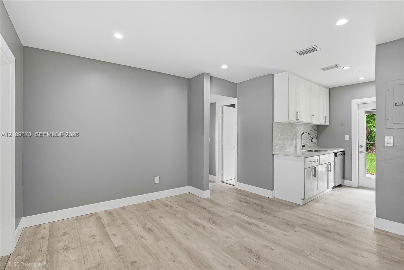 Kitchenette featuring white cabinetry, stone-finish countertops, tile backsplash, and wood-finish flooring Kitchenette featuring white cabinetry, stone-finish countertops, tile backsplash, and wood-finish flooring