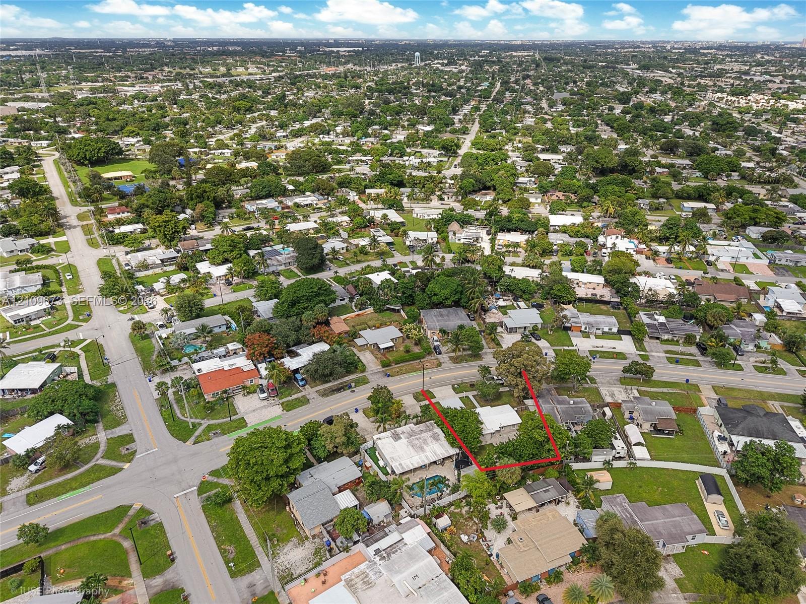 Aerial perspective of a corner lot situated in a suburban residential setting, featuring mature trees and street-level frontage