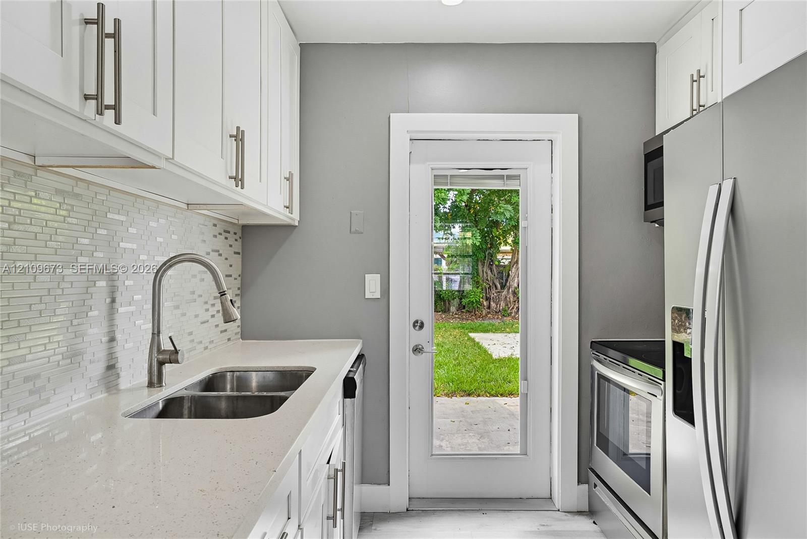 Kitchen featuring white cabinetry, solid-surface countertops, mosaic tile backsplash, stainless steel appliances, and a glass-panel exterior door
