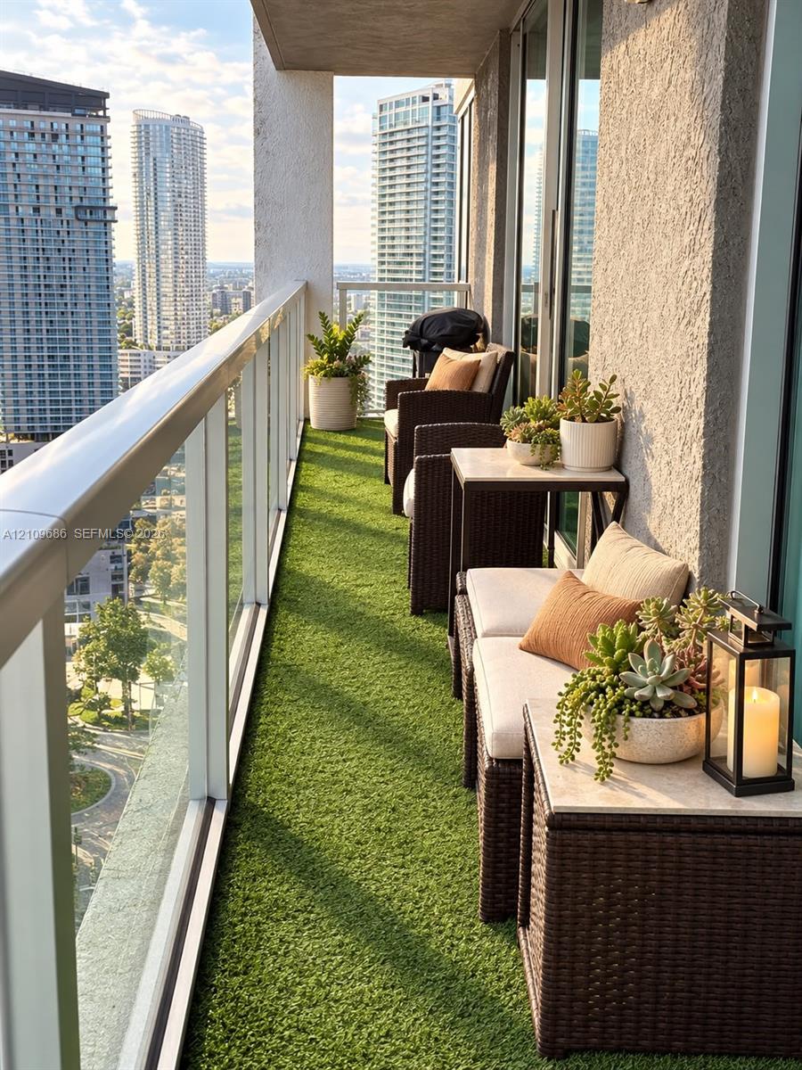 Private balcony featuring synthetic turf flooring, a glass panel railing, and expansive urban skyline scenery