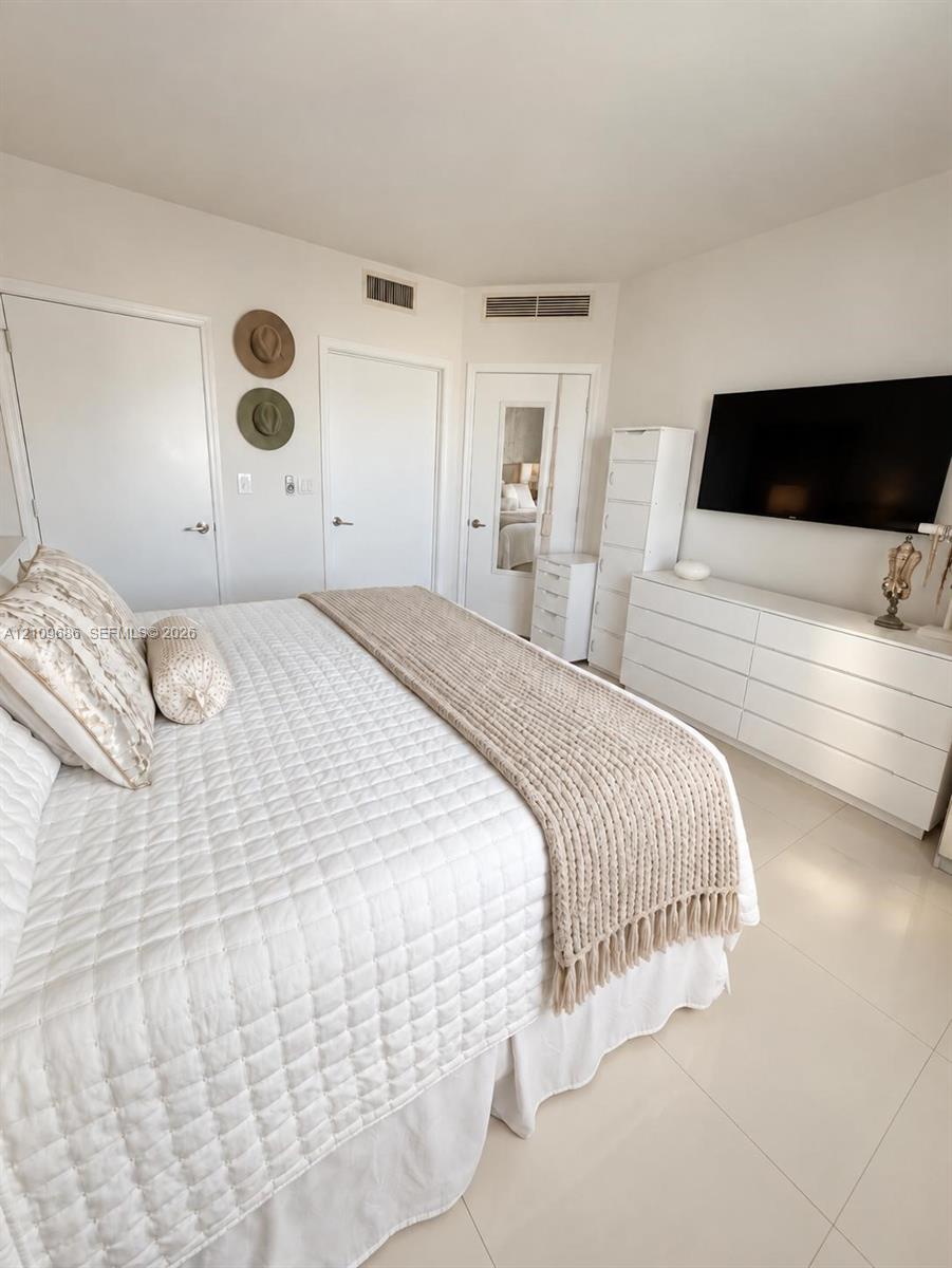 Neutral-toned interior featuring large-format tile flooring, multiple reach-in closets, and a built-in full-length mirror
