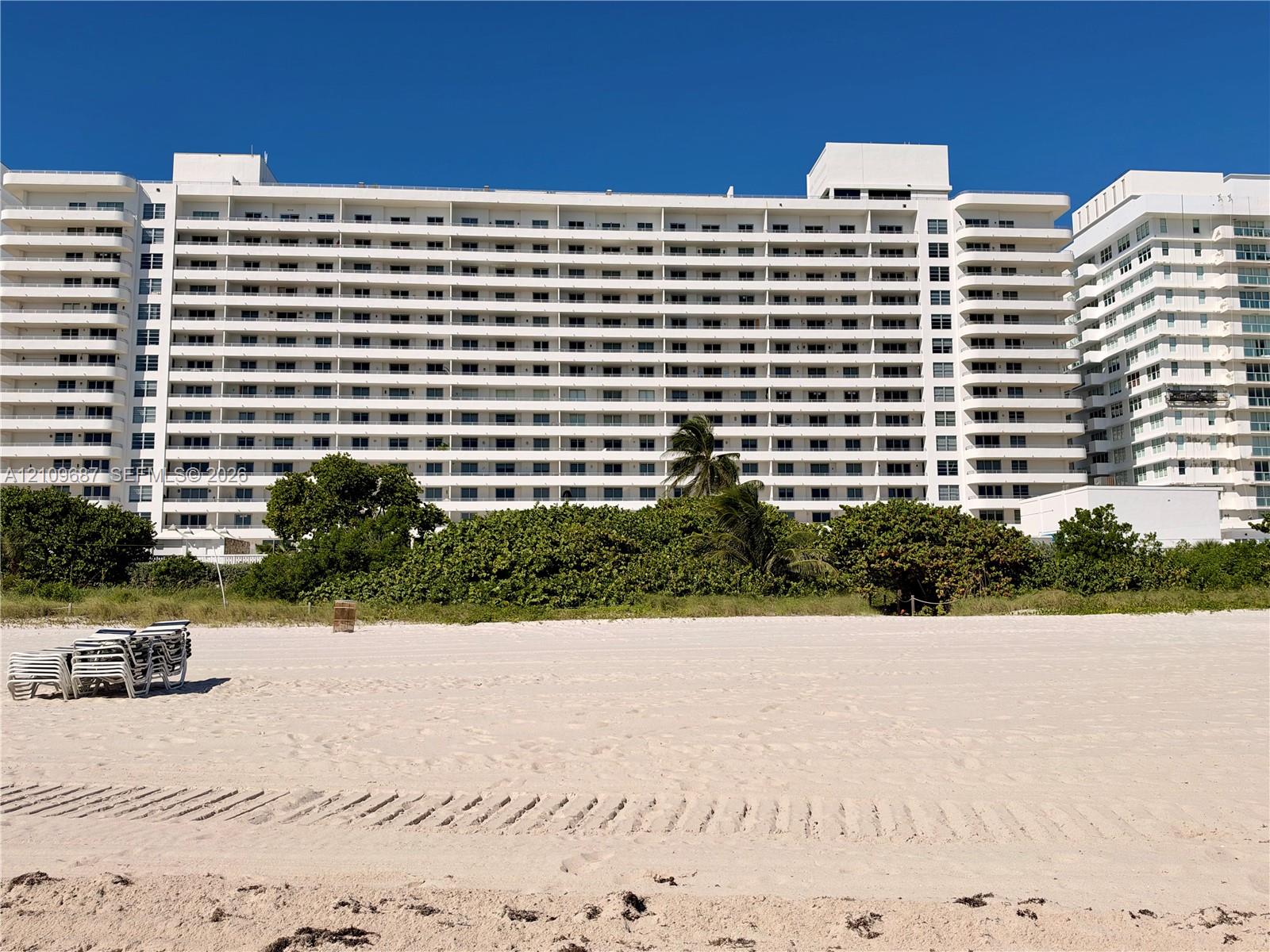 Multi-story white facade high-rise featuring private balconies, floor-to-ceiling glass, direct beach access, and surrounding coastal landscaping