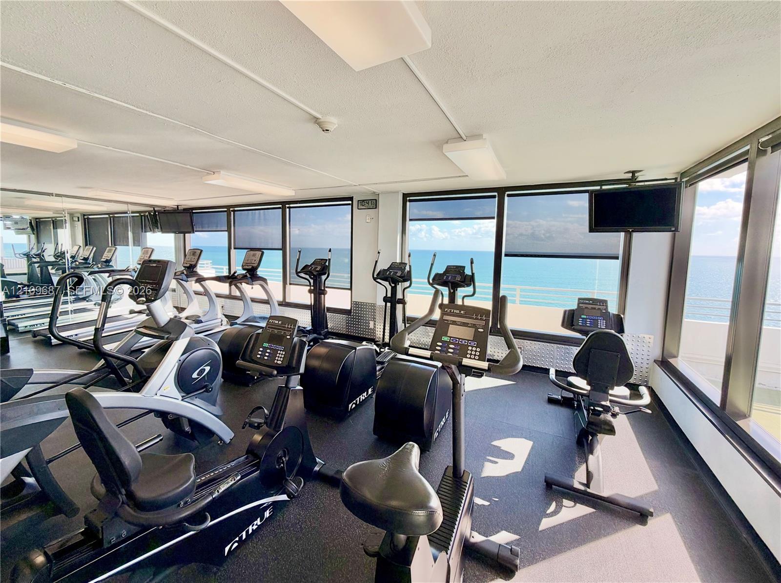 Fitness center featuring rubberized flooring, expansive floor-to-ceiling windows, and wall-mounted televisions