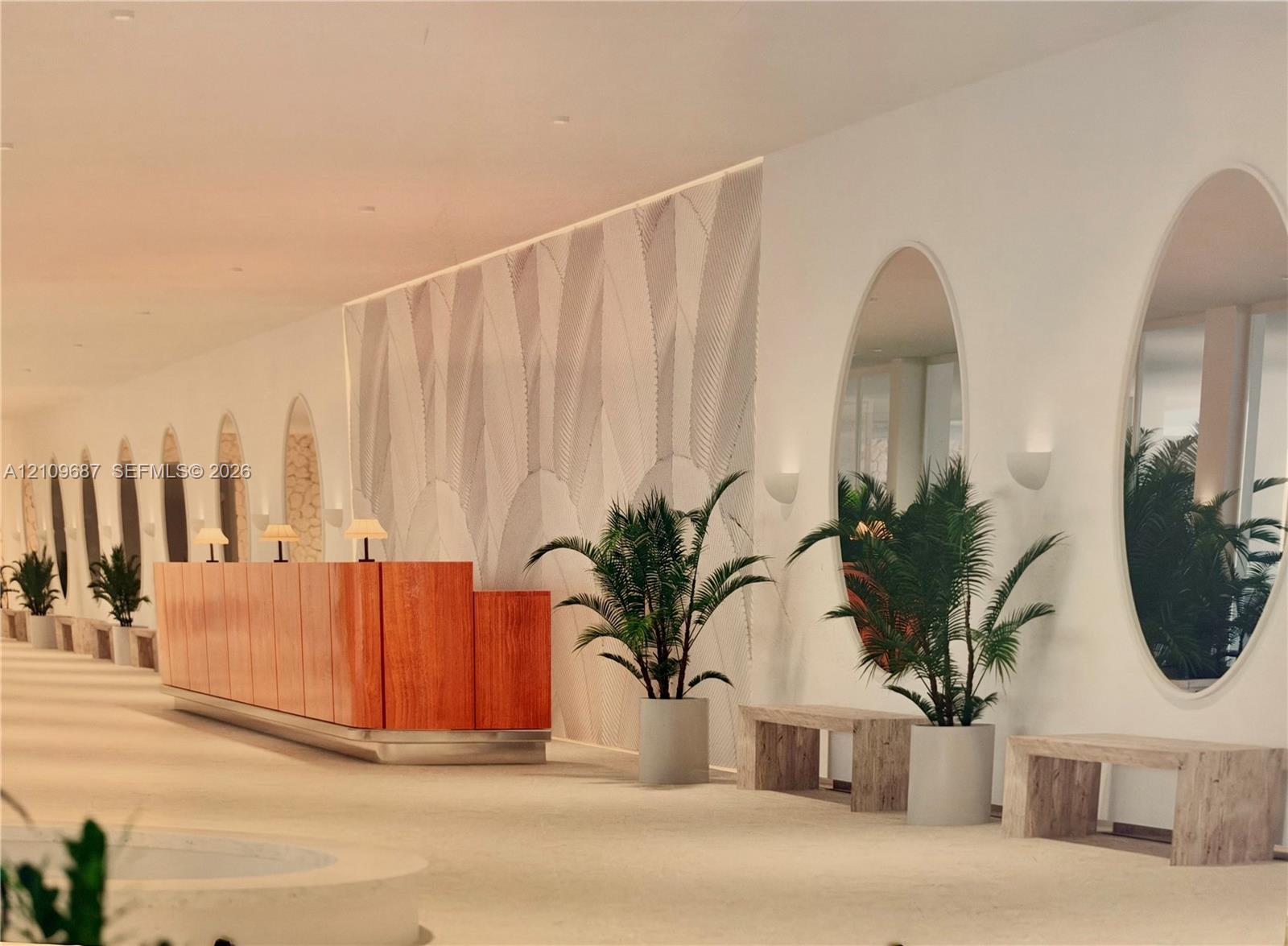 Grand lobby featuring a custom wood-paneled reception desk, full-height oval wall mirrors, decorative wall texturing, and recessed wall-mounted lighting