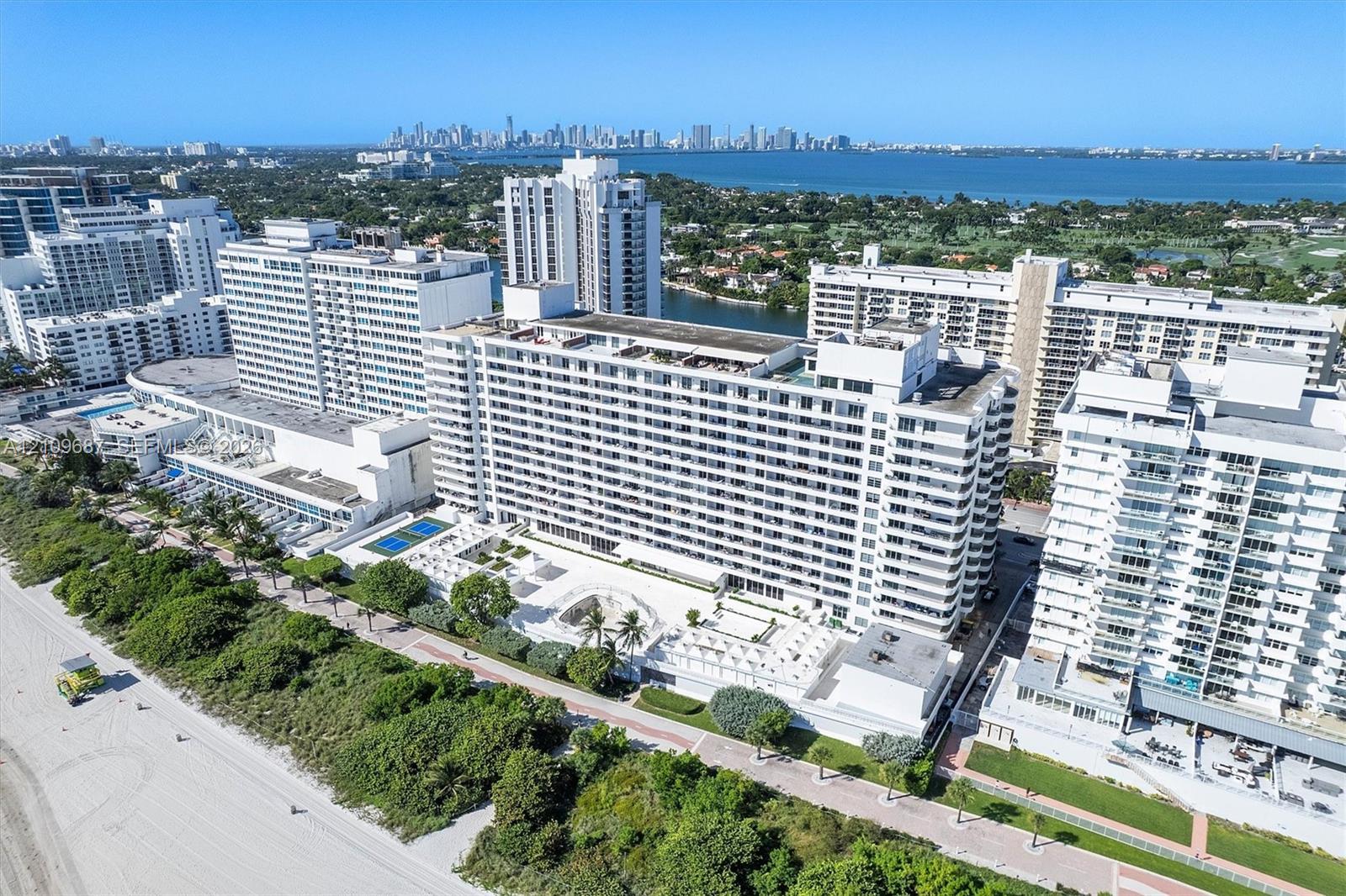 Aerial perspective of coastal high-rise building featuring direct beach access, outdoor swimming pools, multi-purpose sport courts, and expansive shoreline scenery