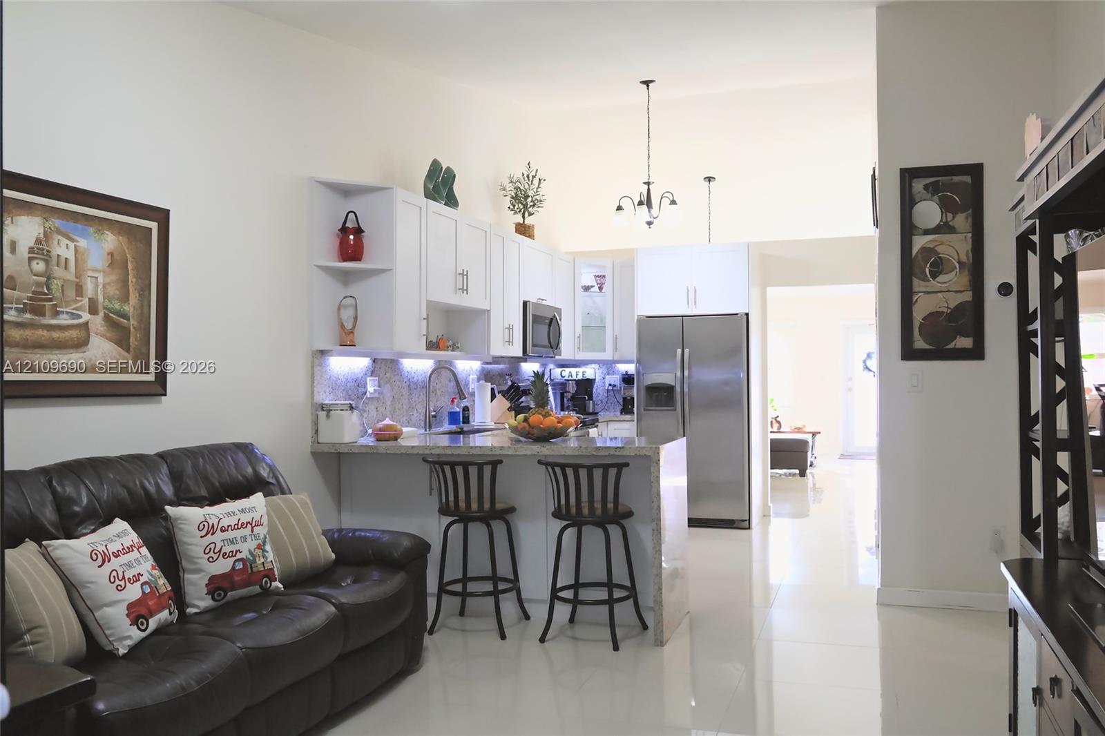 Kitchen featuring white cabinetry, stone-surface countertops, stainless steel appliances, under-cabinet lighting, and a breakfast bar