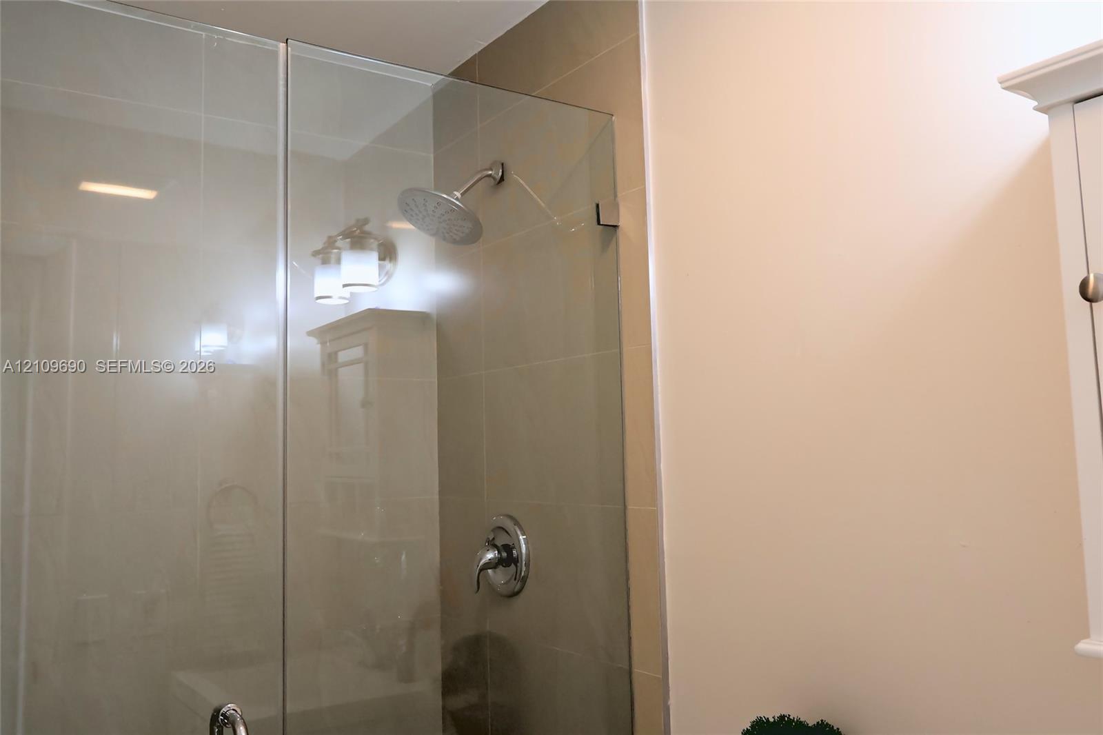 Walk-in shower featuring a glass enclosure, large-format tile wall surround, rainfall showerhead, and single-handle chrome fixture