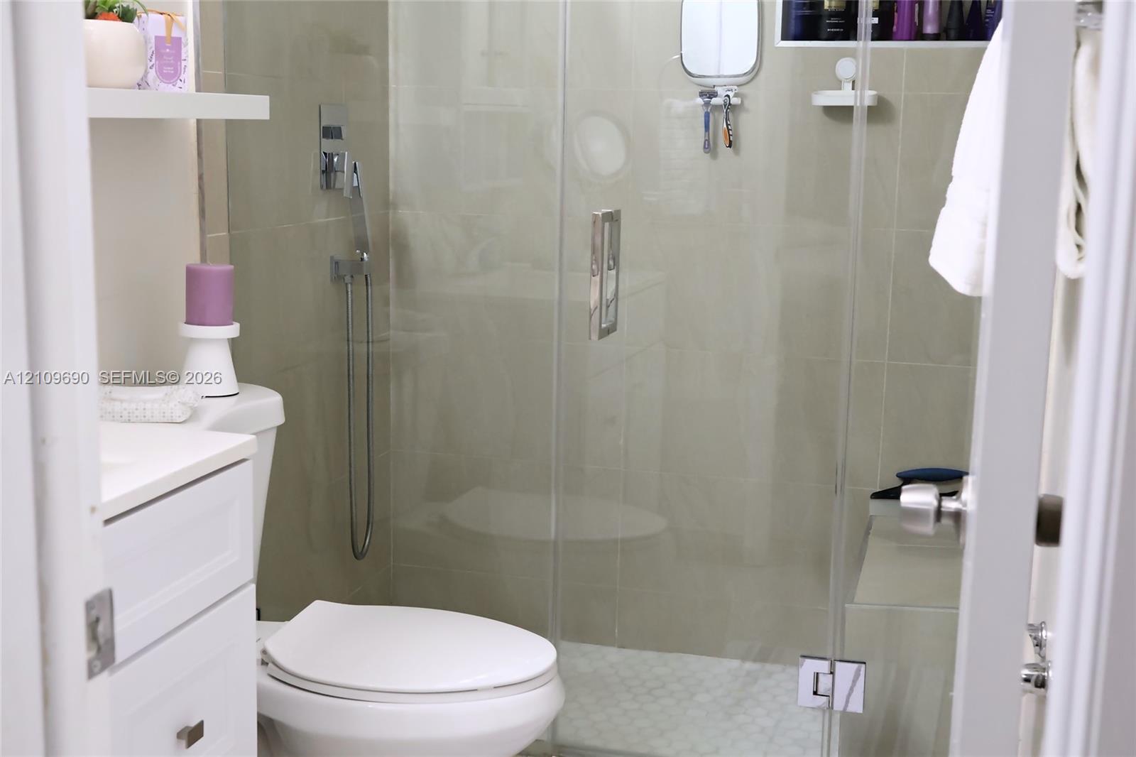 Walk-in shower featuring a frameless glass door, wall-mounted chrome hand-held shower head, integrated tiled shower bench, and pebble-style floor tiling