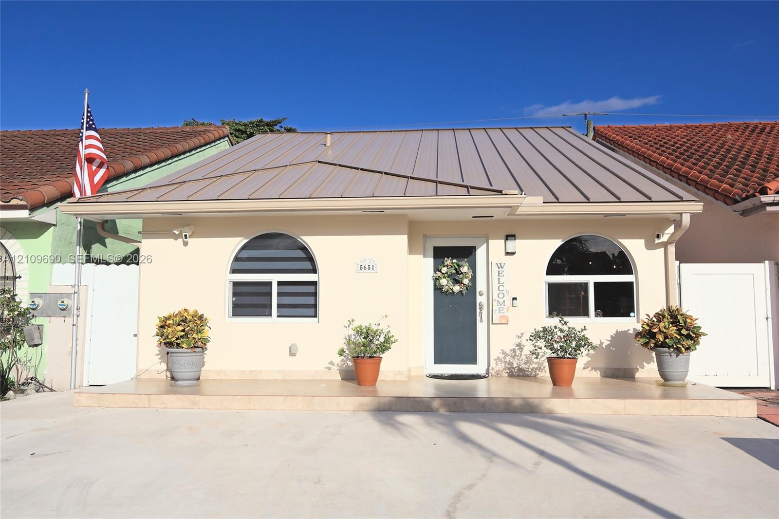 Single-story exterior featuring a metal roof, arched windows, and a tiled front porch Single-story exterior featuring a metal roof, arched windows, and a tiled front porch