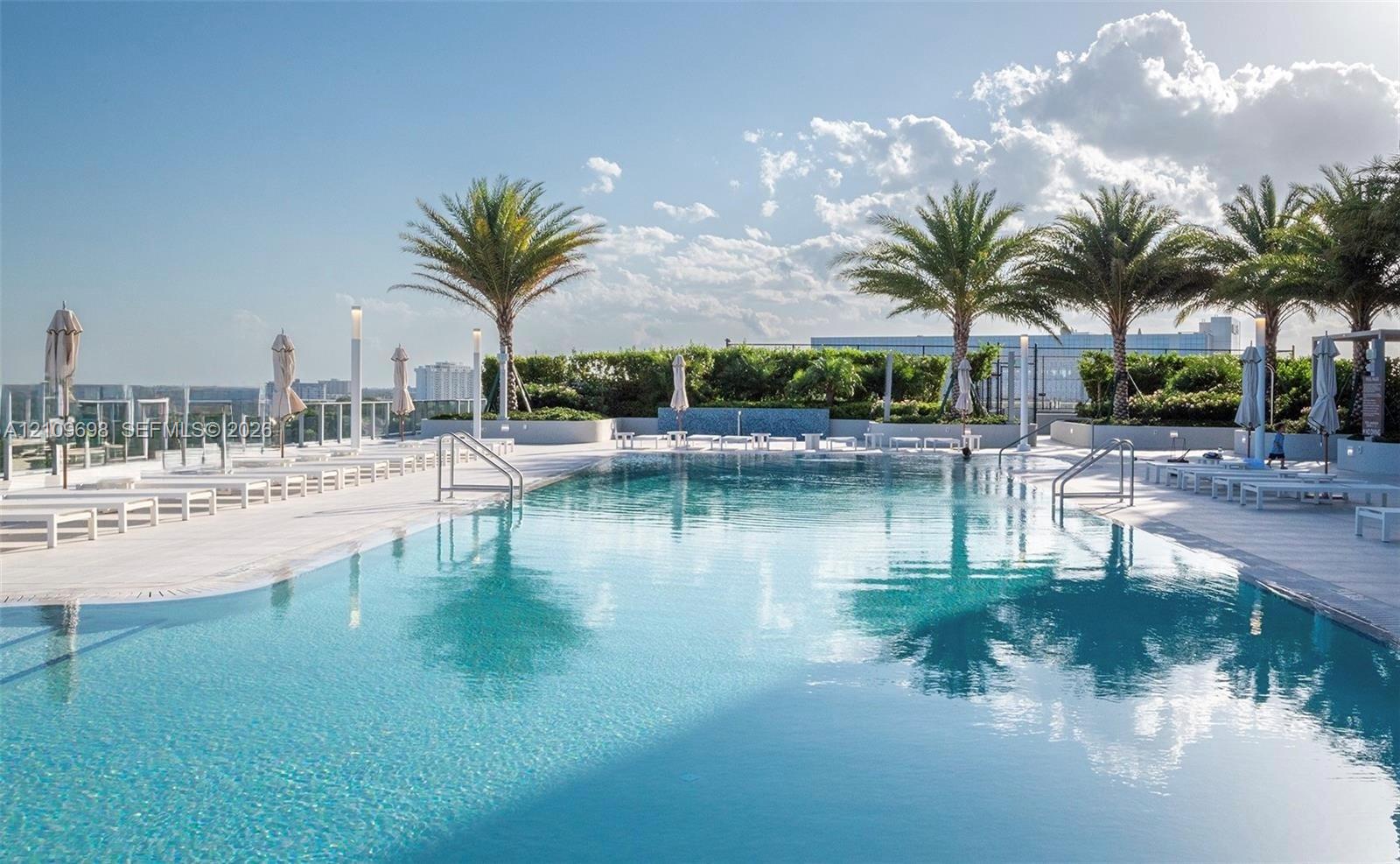 Rooftop swimming pool featuring stone tile decking, perimeter glass railing, built-in water feature, and mature palm trees