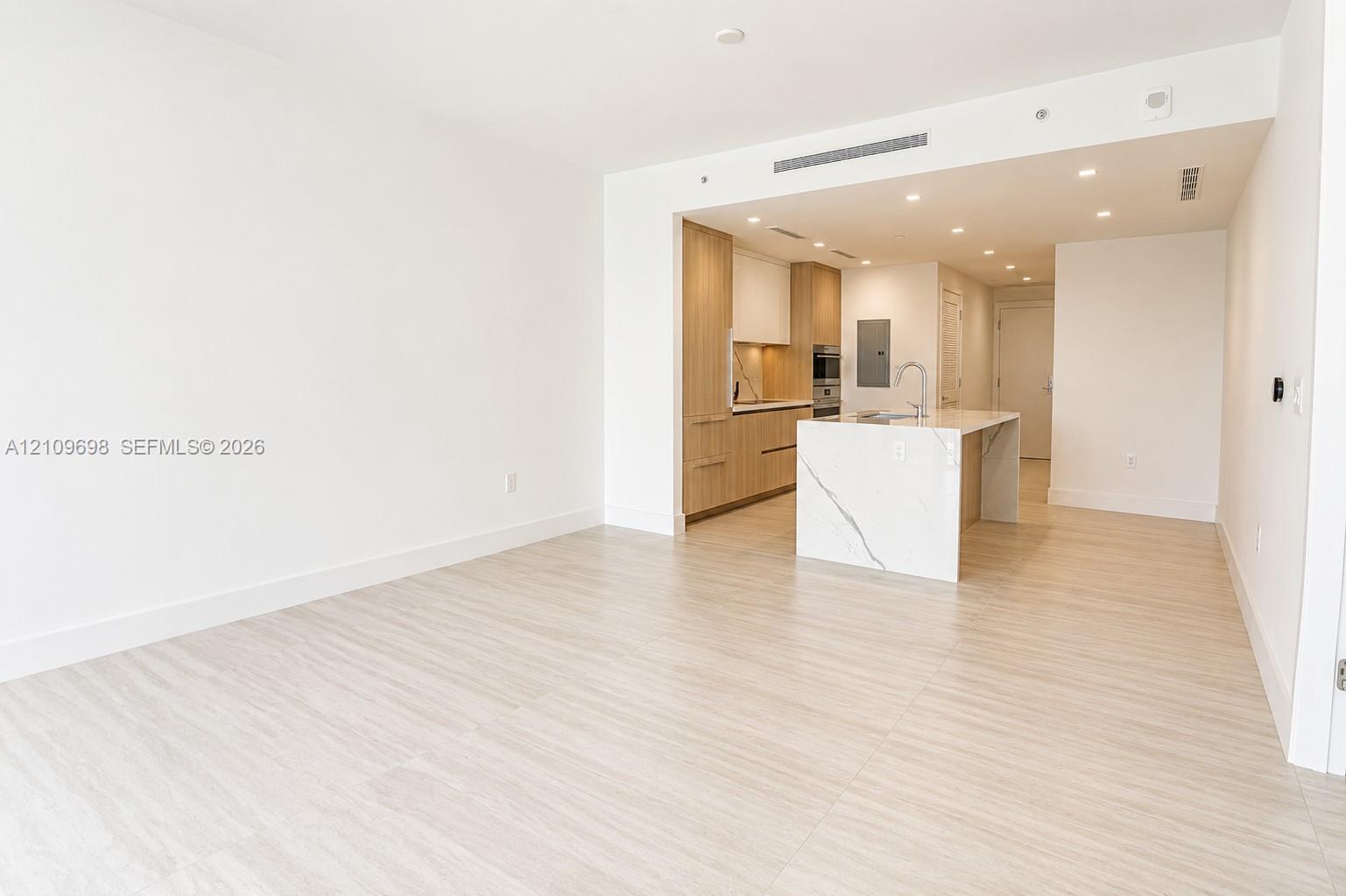 Open-concept kitchen featuring flat-panel wood-finish cabinetry, a waterfall-edge stone island, built-in appliances, recessed lighting, and wood-finish flooring