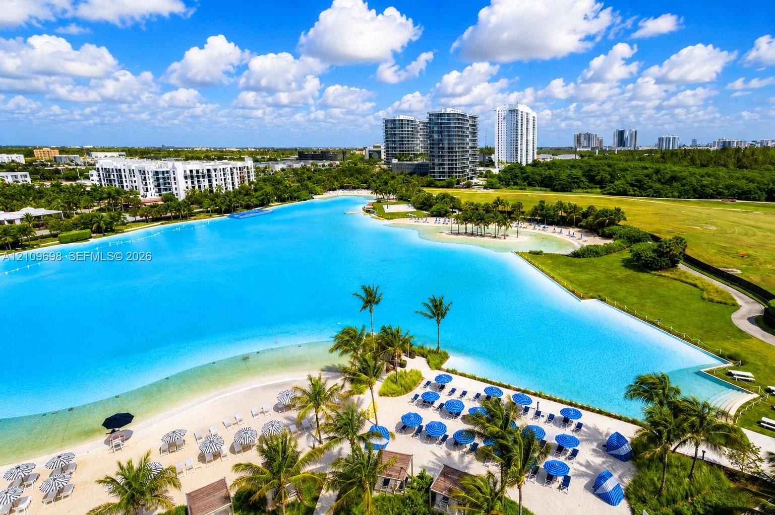 Expansive man-made lagoon featuring a sandy beach, shoreline palm trees, and manicured green space