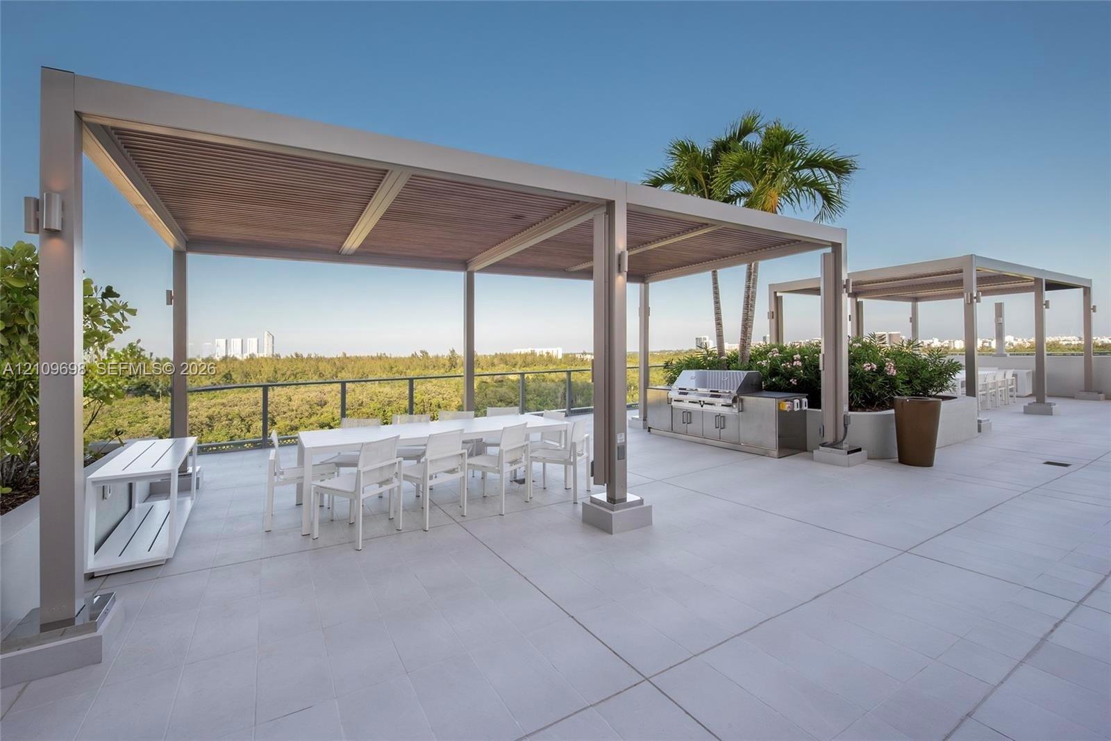 Rooftop terrace featuring large-format tile flooring, dual metal-framed pergolas with wood-finish ceilings, a built-in stainless steel outdoor kitchen, and a glass-panel railing system