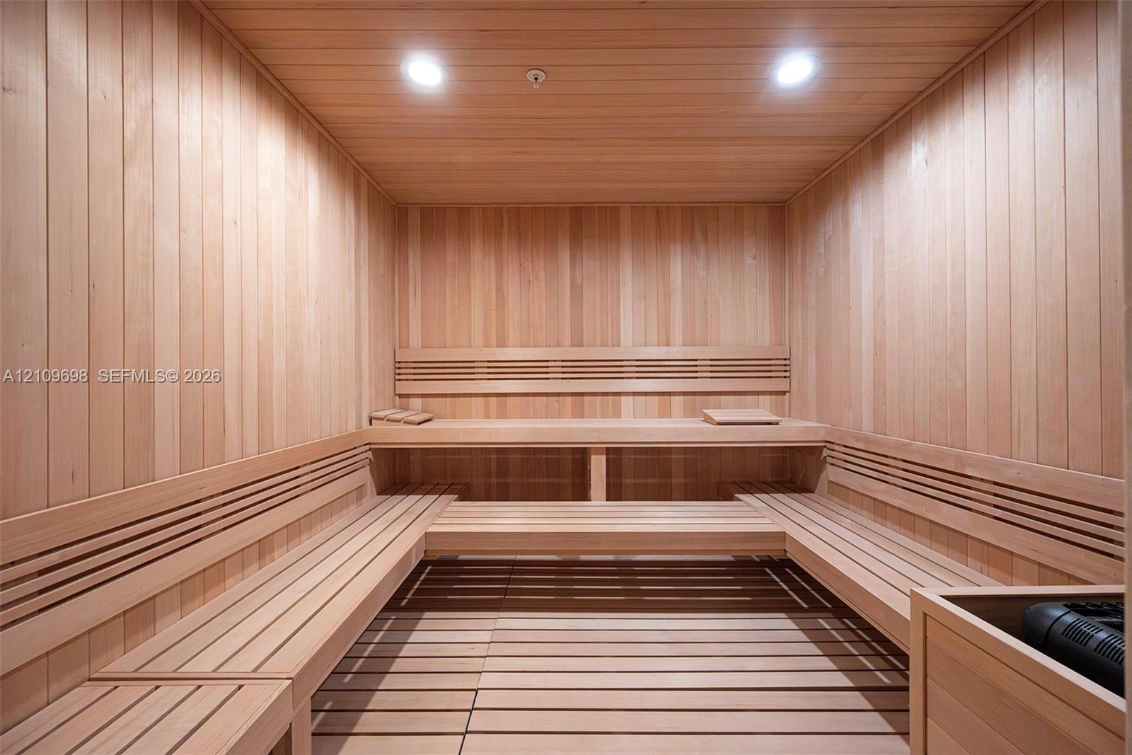 Sauna featuring natural wood-paneled walls, multi-level built-in bench seating, recessed lighting, and a slatted wood floor