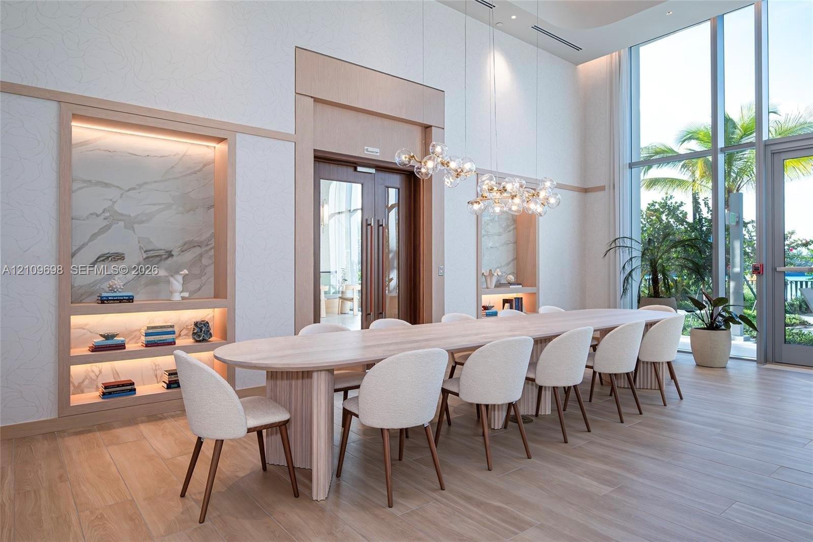 Double-height floor-to-ceiling windows, wood-finish flooring, recessed wall niches with stone accents, integrated accent lighting, and dual suspended modern pendant chandeliers
