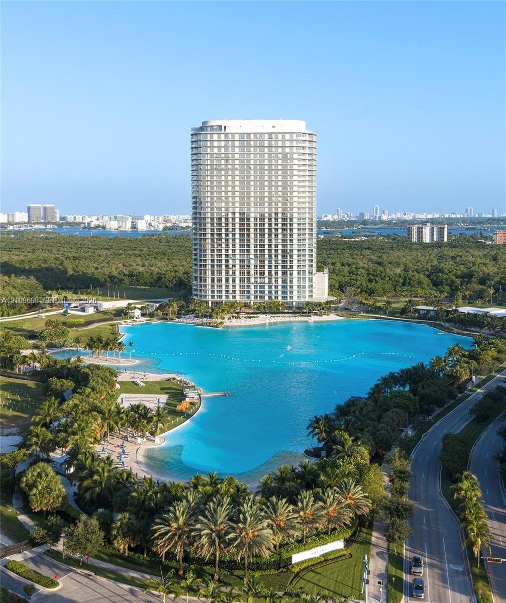 High-rise residential tower featuring floor-to-ceiling windows, expansive man-made lagoon, white sand beaches, and lush tropical landscaping