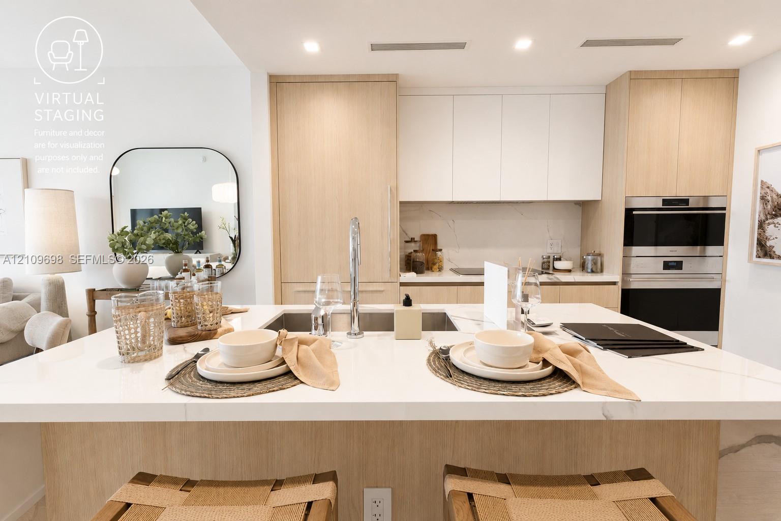 Kitchen featuring an island with a light-toned countertop, custom light-wood cabinetry, matte-finish wall cabinetry, an integrated stainless steel wall oven, and a sleek undermount kitchen sink