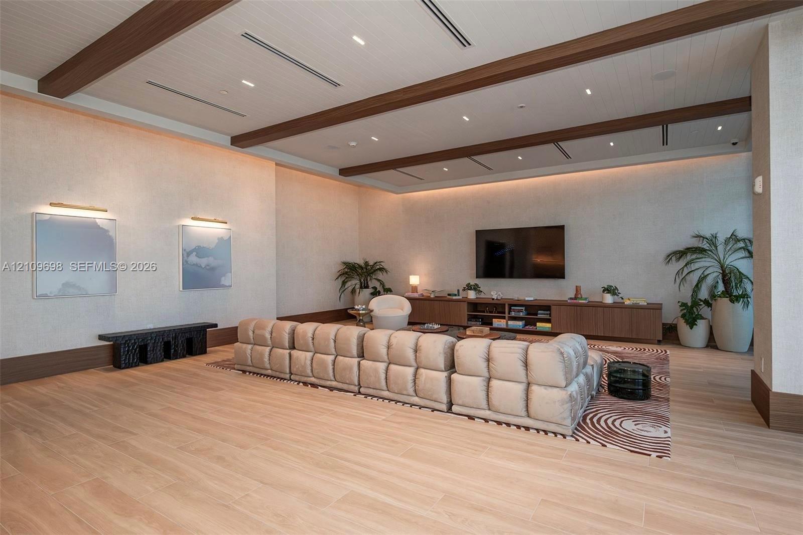 Recessed lighting, wood-finish ceiling beams, wood-finish flooring, built-in media console, and wall-mounted art lighting