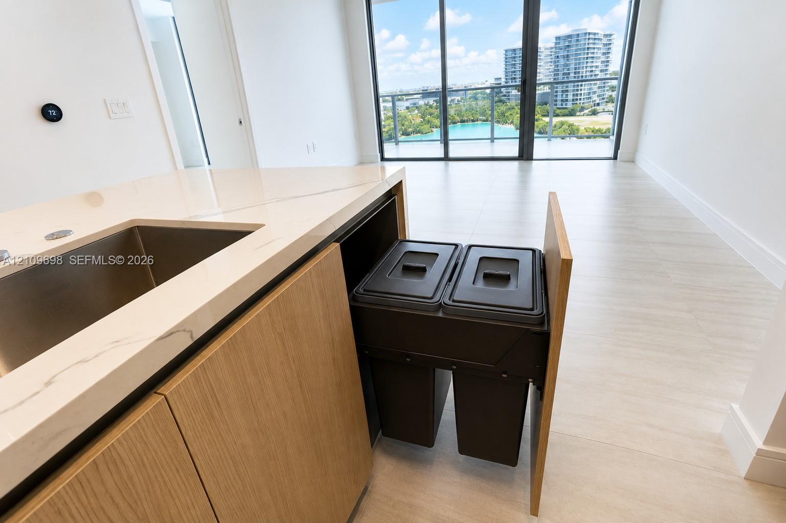 Kitchen island featuring stone-finish countertops, an undermount sink, built-in dual waste disposal cabinetry, and light-tone flooring
